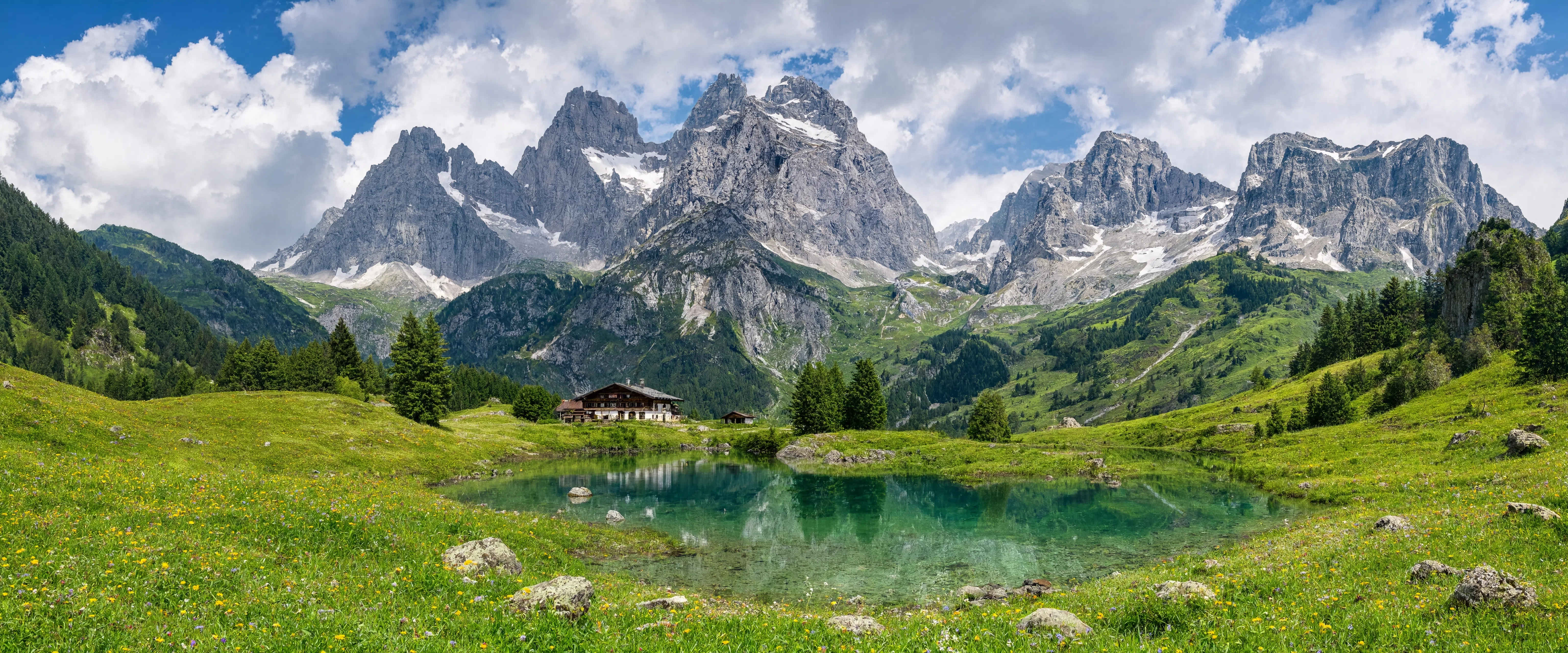 Bayrische Alpenlandschaft mit Bergsee, Wiesen und schneebedeckten Gipfeln im Hintergrund